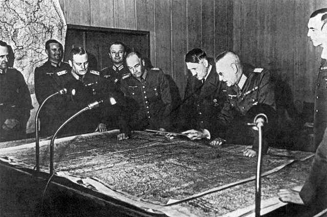 На переднем плане слева направо: командующий Вильгельм Кейтель, полковник В. фон Браухич, Адольф Гитлер и полковник Ф. Гальдер у стола во время заседания генерального штаба.