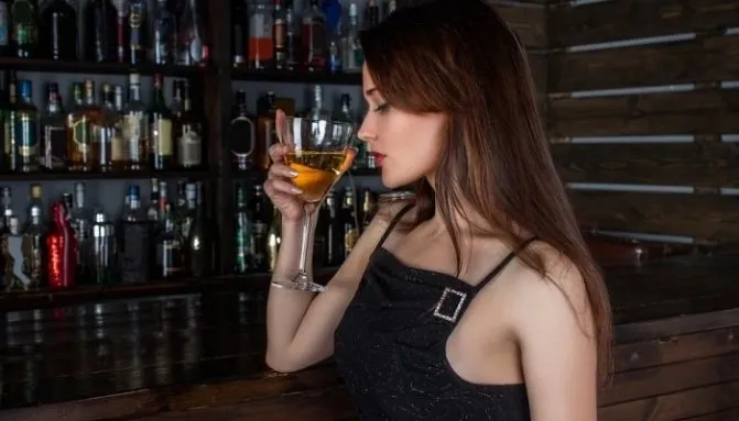 Девушка пьет напиток за барной стойкой