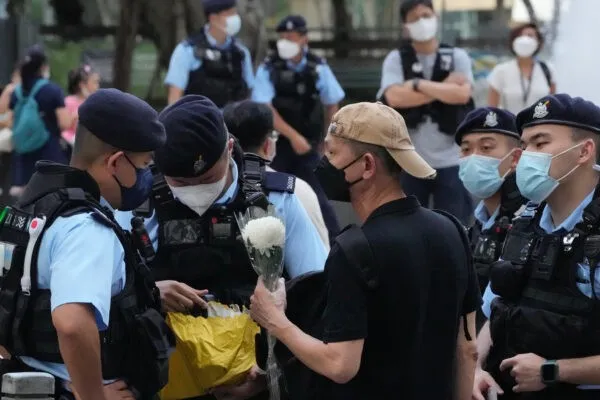 Полицейские обыскивают мужчину с цветком в парке Виктория в Гонконге 4 июня 2022 года. (Kin Cheung/AP Photo)
