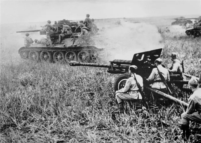 Советский танк Т-34 с десантом на броне проезжает рядом с 76,2-мм дивизионной пушкой ЗиС-3.